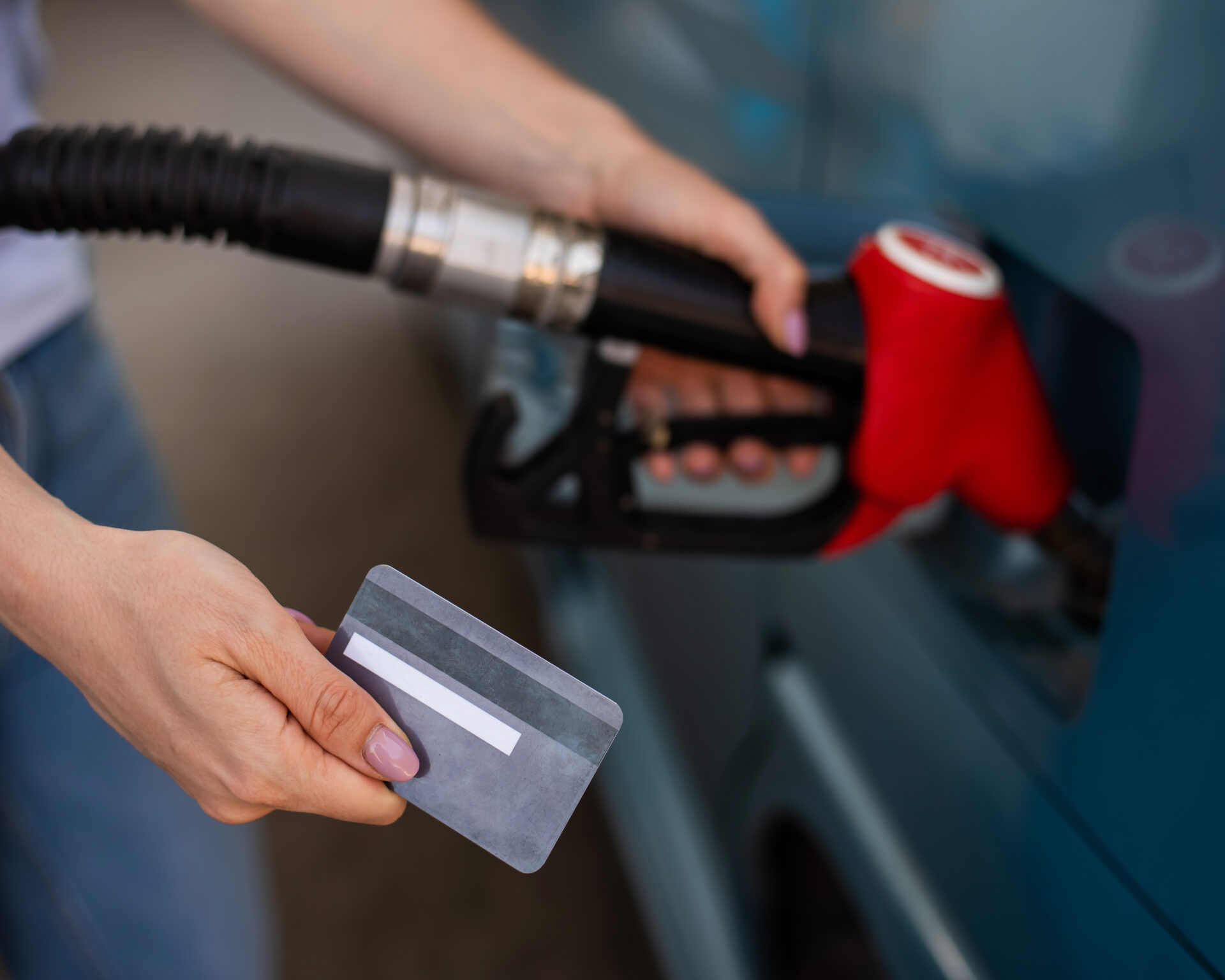 A woman fills her car with gasoline at a self-service gas station and holds a credit card.