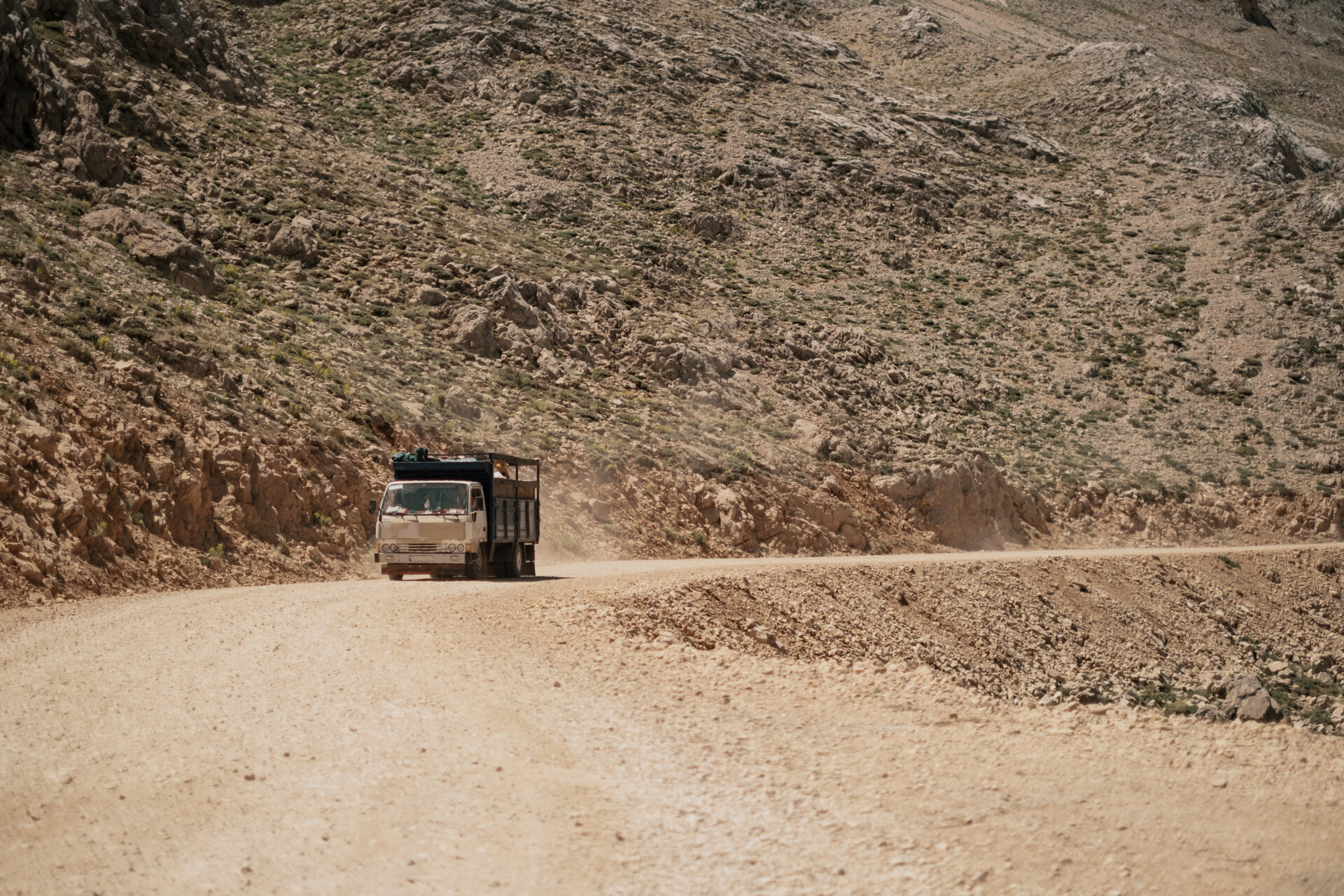 Classic brown big rig semi truck with step down turn on winding road going through the mountains.