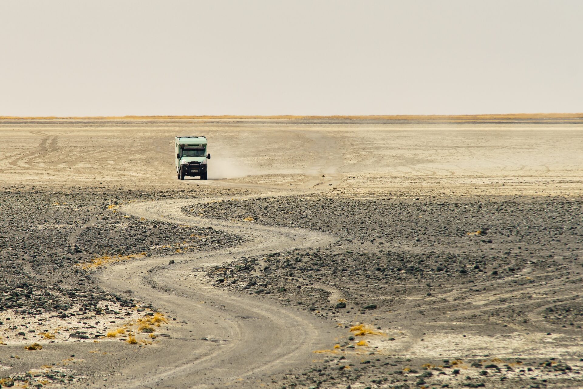 A truck riding through a curvy rocky road making dust